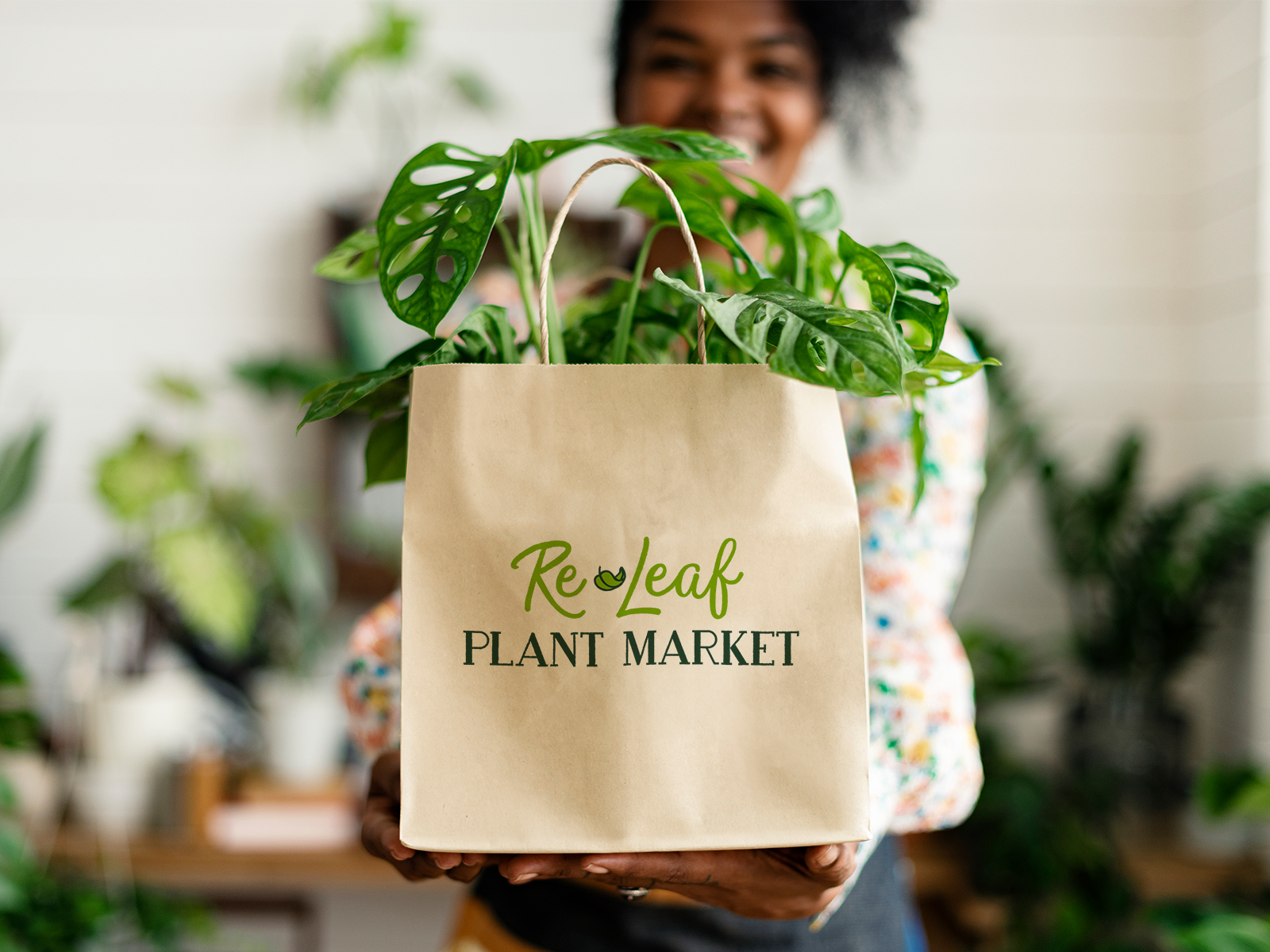 A woman holds a paper bag with a plant in it. The paper bag has a Re-Leaf Plant Market logo.